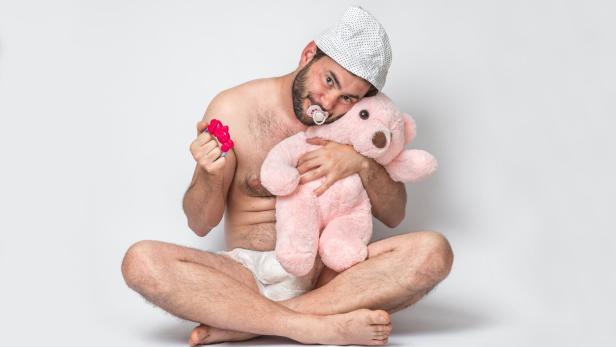 Infant adult man with pacifier in diaper holding pink teddy bear.