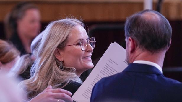 Kronprinzessin Mette-Marit von Norwegen lächelt ihrem Ehemann Kronprinz Haakon zu, während sie gemeinsam ein Blatt Papier mit Text lesen.