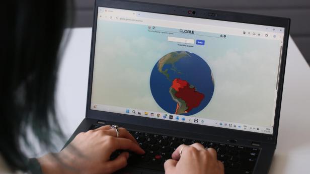 Person tippt auf einem Laptop ein Geografie-Spiel mit einer farbigen Weltkarte.