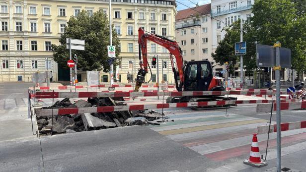 Bagger bei Straßenbau an einer gesperrten Kreuzung mit aufgerissener Fahrbahn.