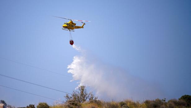 Gelber Löschhubschrauber wirft Wasser über einer Brandstelle ab.