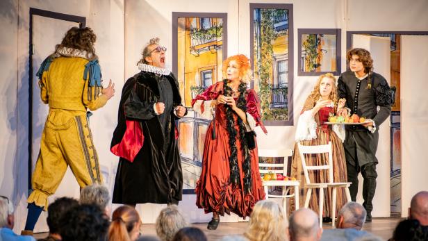 Historische Theateraufführung mit fünf kostümierten Schauspielern vor sitzendem Publikum.