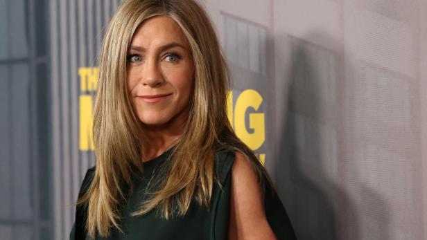 Jennifer Aniston lächelt vor einem Hintergrund mit dem Schriftzug „The Morning Show“.