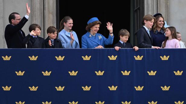 Die schwedische Königsfamilie mit Königin Silvia winkt von einem mit Kronen verzierten Balkon des Stockholmer Schlosses der Menge zu.