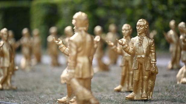 Zahlreiche goldene Mozart-Statuen stehen in einer Parkanlage auf einer Wiese.