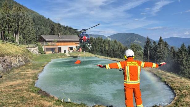 Ein Feuerwehr-Flughelfer weist einen Hubschrauber über einem Wasserbecken in den Bergen ein.