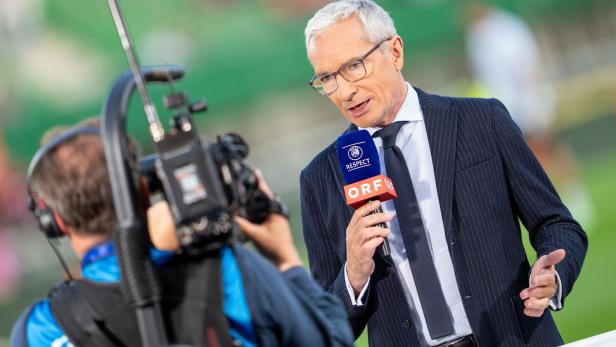 Moderator Rainer Pariasek steht mit Mikrofon vor einem Kameramann und macht eine Moderation