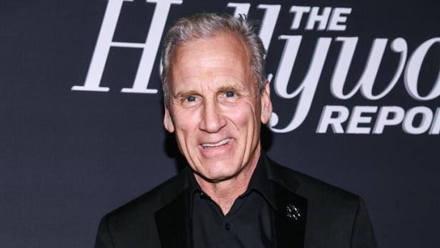 Der Schauspieler Will Roberts lächelt vor einem Hintergrund von The Hollywood Reporter in einem schwarzen Anzug.