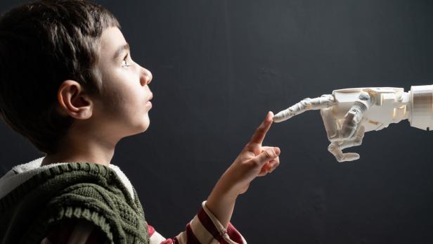 Ein Junge berührt neugierig mit dem Finger die Spitze eines Roboterfingers.