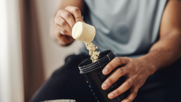Person adding protein powder to shaker for fitness