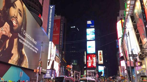 Ein belebter Times Square bei Nacht mit einer großen Werbetafel von Conchita Wurst.