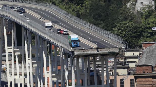 Hochgelegte Autobahnbrücke mit mehreren Fahrzeugen über einem Tal und Gebäuden darunter.
