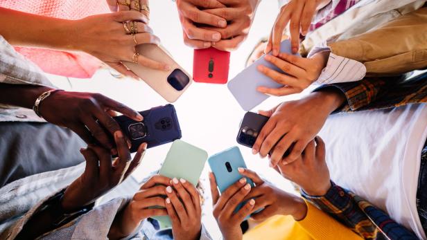 Mehrere Personen halten ihre Smartphones in einem Kreis zusammen, wobei die Bildschirme nach innen gerichtet sind.