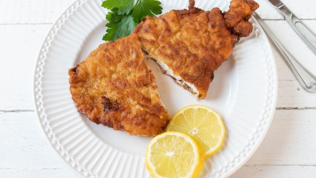 Breaded chicken schnitzel with lemon and parsley isolated on a white plate on white background.