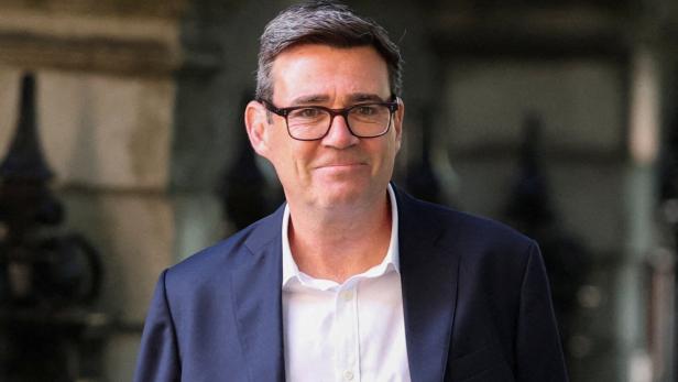 Andy Burnham trägt ein weißes Hemd und ein dunkelblaues Sakko sowie eine Brille.