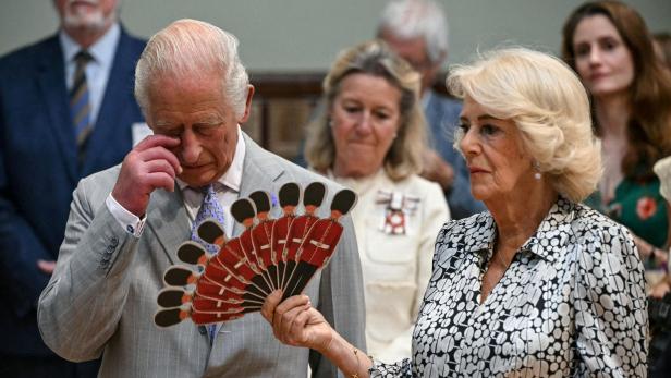 König Charles III. wischt sich eine Träne aus dem Auge, während Königin Camilla einen Fächer mit Motiven britischer Gardesoldaten hält.