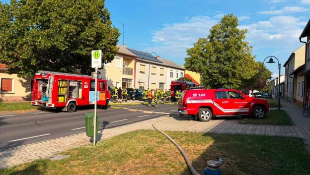 Feuerwehrkräfte und Einsatzfahrzeuge sichern eine Straße mit ausgelegtem Schlauch vor Wohnhäusern.
