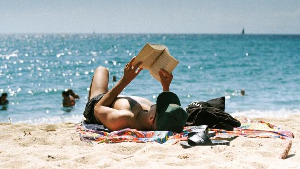 Person liest entspannt am Strand in der Sonne.