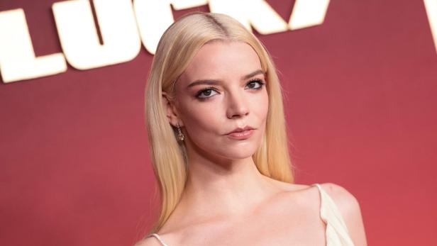 Anya Taylor-Joy mit blondem Haar vor einem roten Hintergrund.