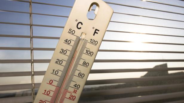 Thermometer vor Jalousien zeigt sonnig-warme Außentemperatur an.