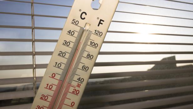 Thermometer vor Jalousien zeigt sonnig-warme Außentemperatur an.