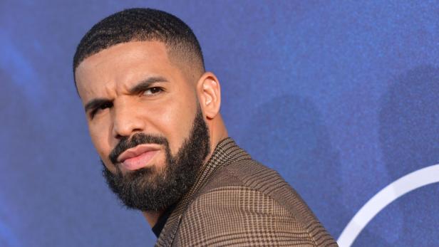 Der Rapper Drake blickt mit kurzem Haar und gepflegtem Bart vor einem blauen Hintergrund zur Seite.