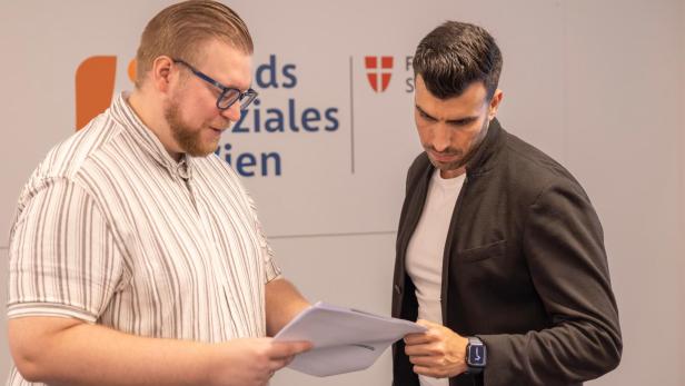 Zwei Männer besprechen Unterlagen vor dem Fonds-Soziales-Wien-Logo.