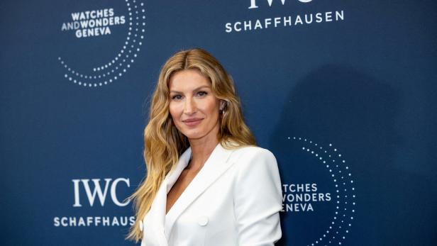 Gisele Bündchen posiert vor einer blauen Wand mit Logos von IWC Schaffhausen und Watches and Wonders Geneva.