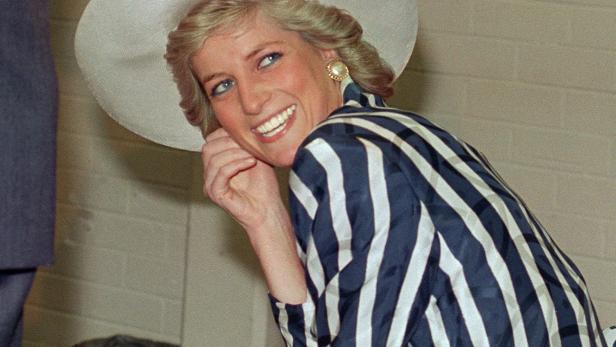 Prinzessin Diana lächelt in einem blau-weiß gestreiften Kostüm und einem passenden weißen Hut.
