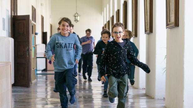 Kinder laufen fröhlich durch einen Klostergang.