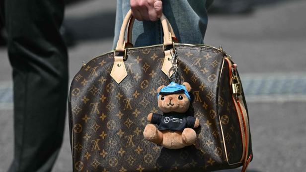 Eine Hand hält eine Louis-Vuitton-Tasche mit Teddybär-Anhänger im Mercedes-AMG-Petronas-Outfit.