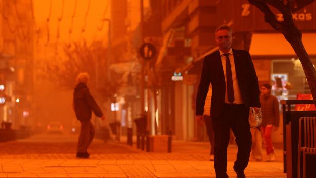 Ein Mann im Anzug mit Schutzmaske geht auf einer Straße in Heraklion auf Kreta. Die Luft ist durch Sahara-Staub orange gefärbt. 