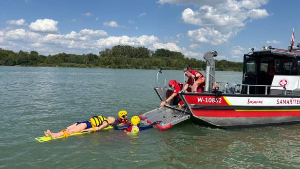 Zwei Rettungsschwimmer in gelben Helmen bergen eine Übungspuppe auf einer Trage vom Rettungsboot „Susanne“ der Samariter aus dem Wasser.