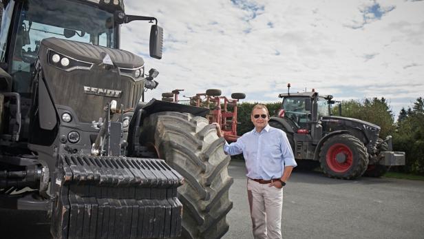 Mann in hellblauem Hemd steht neben großem Fendt-Traktor auf einem Hof.