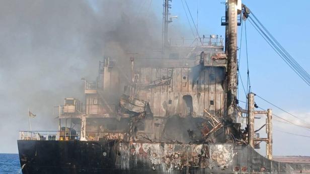Rauchender, stark beschädigter Schiffsrumpf auf dem Meer.