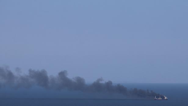 Ein Schiff auf ruhiger See stößt eine lange schwarze Rauchfahne aus.