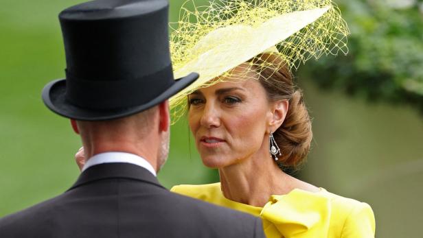 Prinzessin Kate trägt ein gelbes Kleid und einen auffälligen Hut, während sie mit William im Zylinder spricht.
