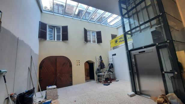 Innenhof mit Glasdach, alten Fenstern, großer Holztür und Aufzugsschacht während Renovierungsarbeiten.