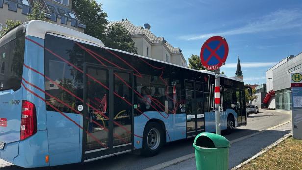 Stadtbus hält an Haltestelle neben Parkverbotsschild und grüner Mülltonne.