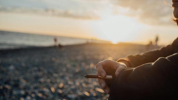 Person sitzt am Strand mit Zigarette