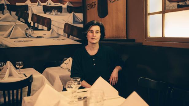 Eine Frau sitzt in einem gemütlichen Restaurant an einem gedeckten Tisch mit weißen Servietten.