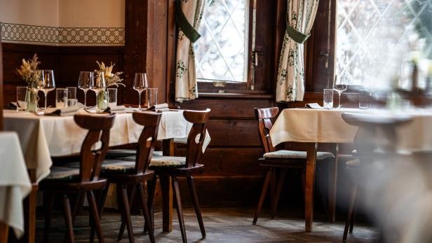 Gemütliches Restaurant mit gedeckten Tischen, Holzstühlen und großen Fenstern.