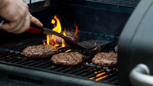 Grill mit brennenden Flammen und Hamburgern auf dem Rost.