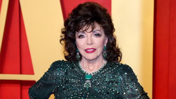 Joan Collins trägt ein funkelndes, smaragdgrünes Abendkleid vor einem roten Hintergrund.