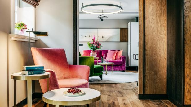 Elegantes Wohnzimmer mit rosafarbenem Sessel, grünen und pinken Sofas, Blumen und modernen Tischen.