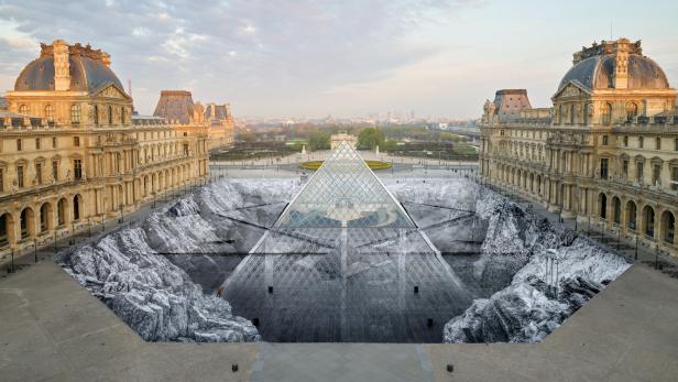 Die Glaspyramide des Louvre in Paris ist von einer großflächigen, schwarz-weißen Bodeninstallation umgeben, die eine felsige Landschaft darstellt.
