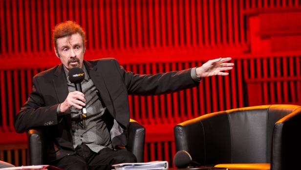 Ein Mann mit Bart spricht in ein Mikrofon von radioeins und gestikuliert vor einem roten Hintergrund.