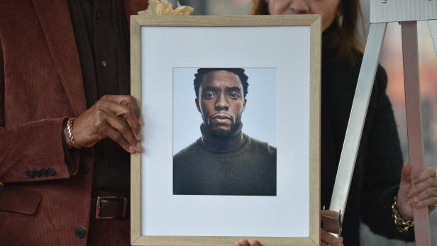 Personen halten einen gerahmten Porträtabzug des verstorbenen Schauspielers Chadwick Boseman in den Händen.
