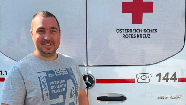Mann lächelt vor einem Rettungswagen des Österreichischen Roten Kreuzes und zeigt den Daumen hoch.