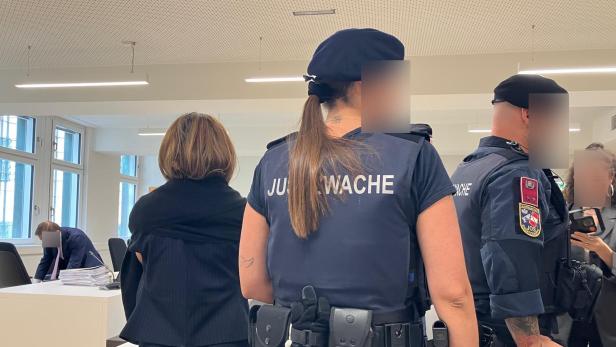 Justizwachebeamte im Gerichtssaal neben einer Frau am Tisch.